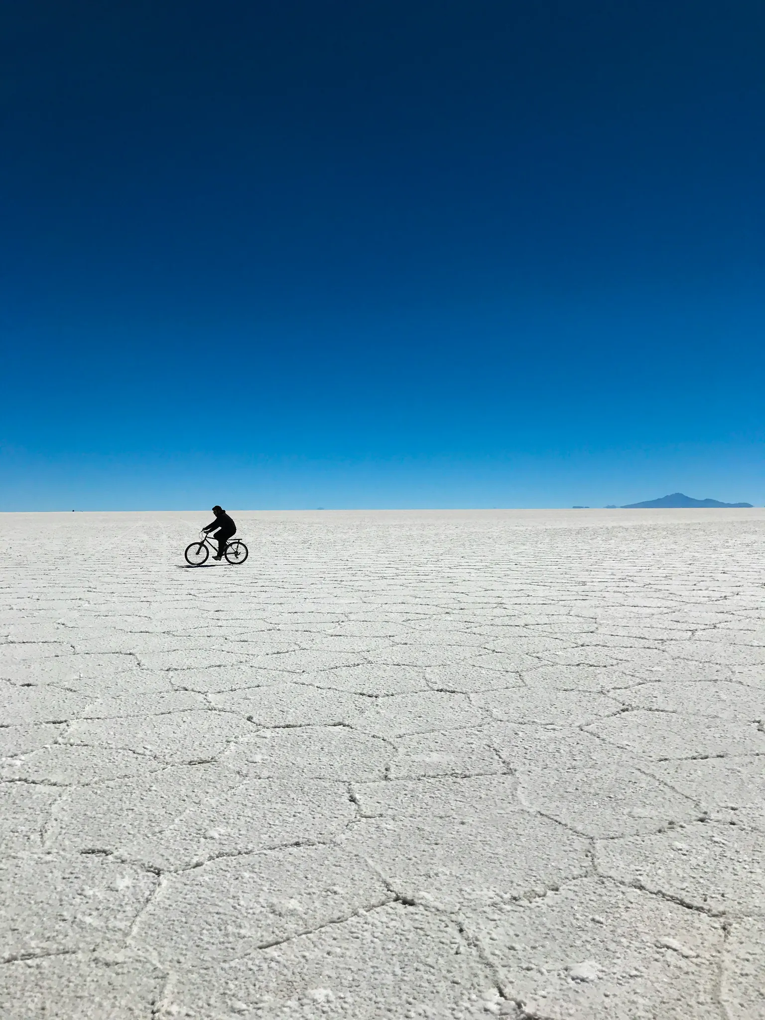 Ciclista pedalando sozinho sobre o chão de sal em hexágonos do Salar de Uyuni, na Bolívia, sob um céu azul profundo