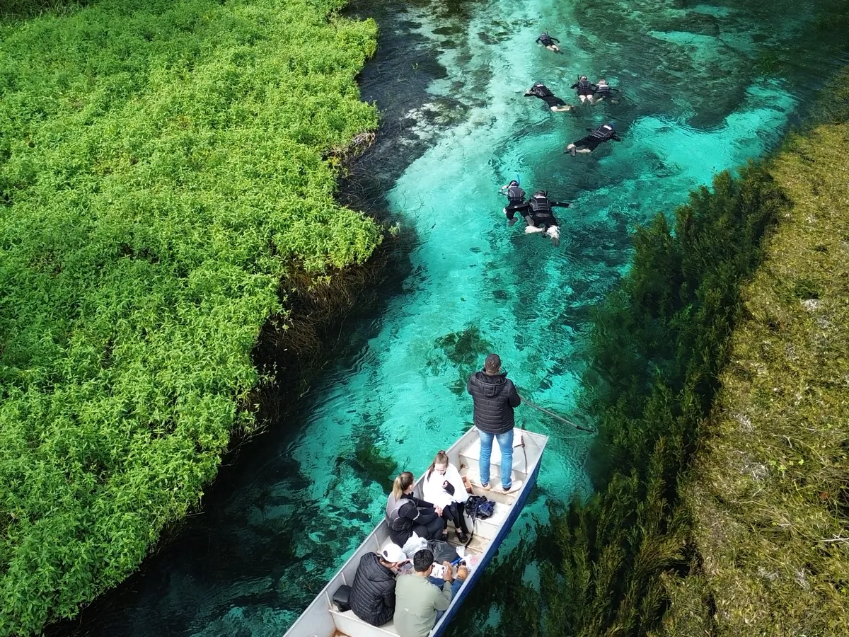 Vista aérea de viajantes flutuando no rio de águas azul-turquesa, com o barco de apoio, em Bonito
