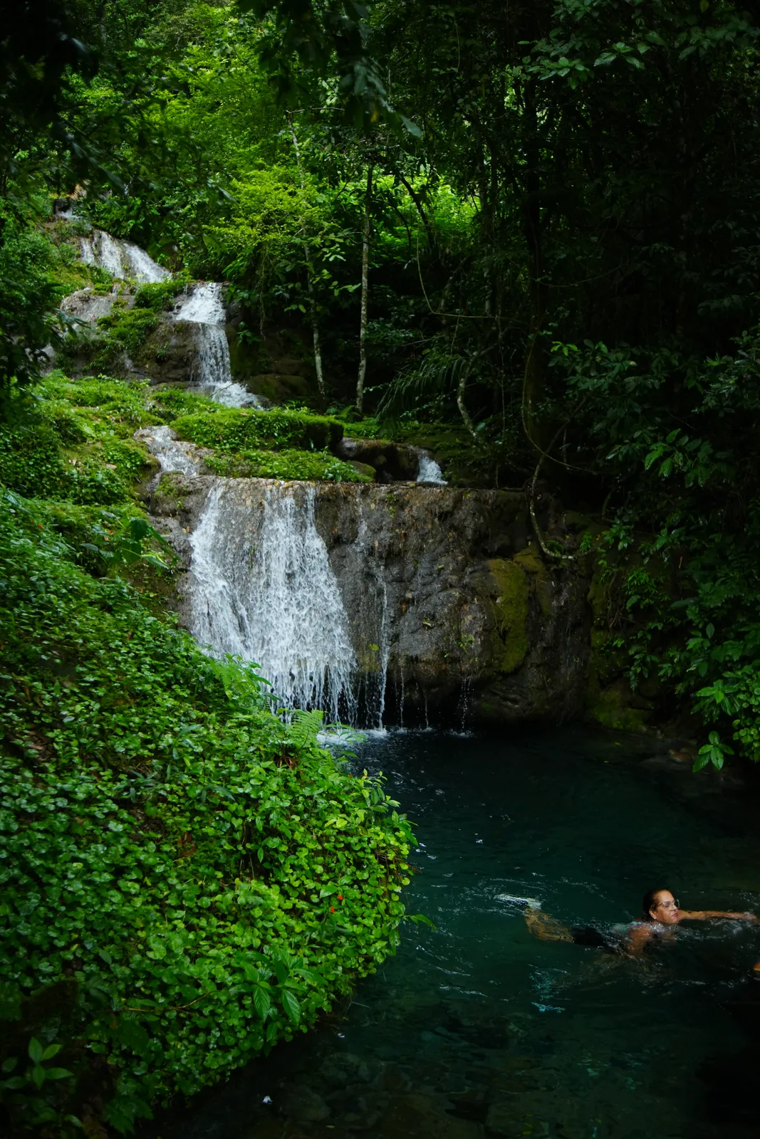 Cachoeira em degraus no meio da mata, com uma pessoa nadando no poço, em Bonito