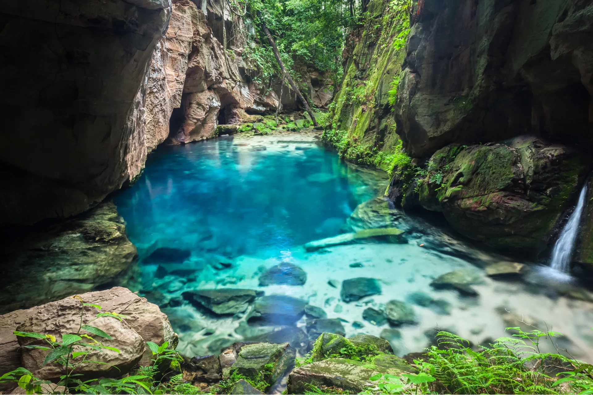 Poço de água azul-turquesa cercado por paredões de pedra e vegetação na Chapada das Mesas