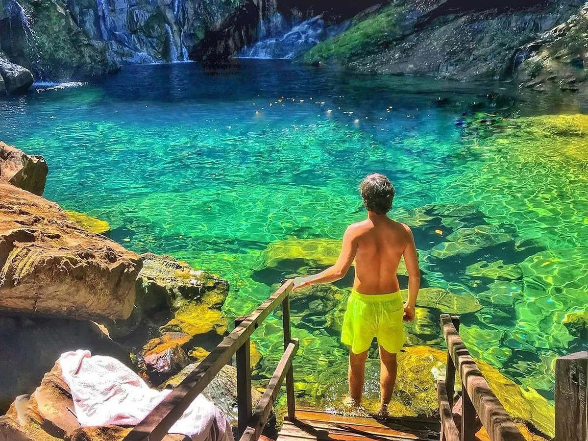 Viajante descendo a escada de madeira até um poço de água azul-turquesa cristalina, na Chapada das Mesas