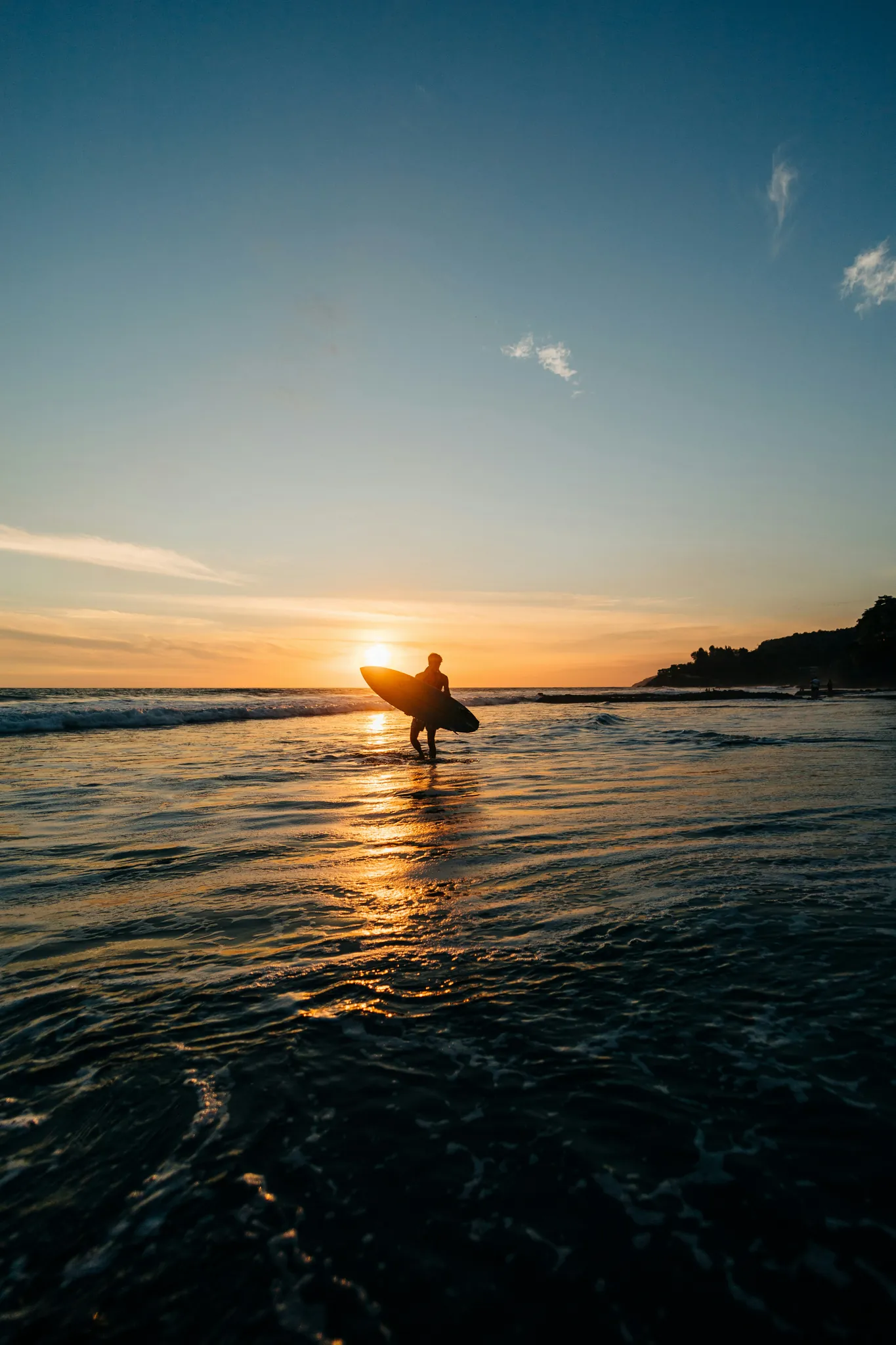 Surfista com a prancha saindo do mar contra a luz do pôr do sol, em El Salvador