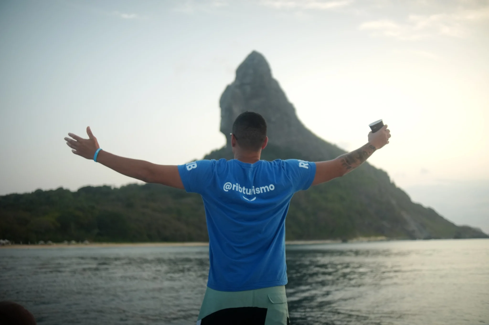 Viajante de braços abertos diante do Morro Dois Irmãos em Fernando de Noronha